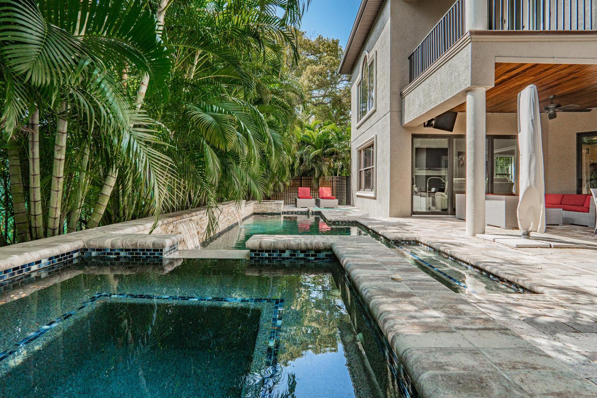 Lush landscaped pool at 2906 West Hawthorne Road. Palm trees and lush greens hang near and shade a blue pool and spa in the backyard next to a tall, gated home.
